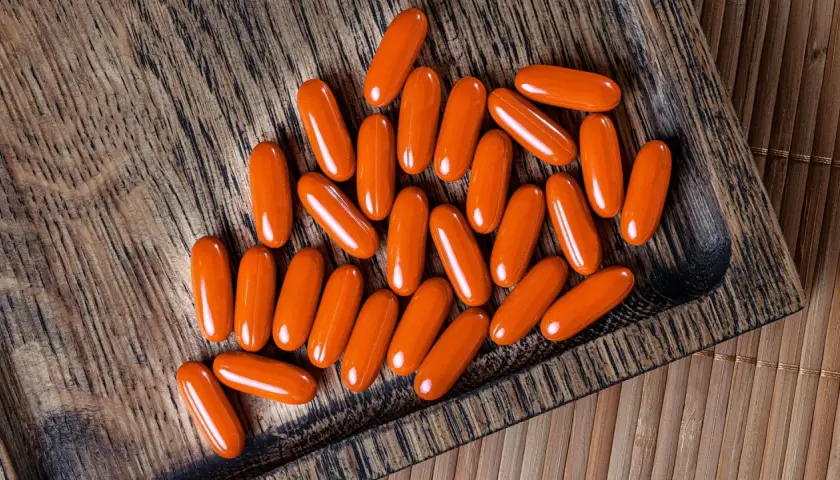Orange Kapseln mit Beta-Carotin liegen auf einem Holzbrett. Sie könnten Rauchern helfen, ihre Lungen zu schützen.