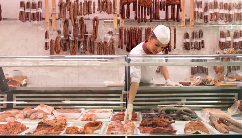 Fleischtheke mit Wurst und Fleischwaren. Eine Verkäuferin sortiert Ware. Hier findet man Inspiration, wie viel Fleisch pro Woche auf dem Teller landen könnte.