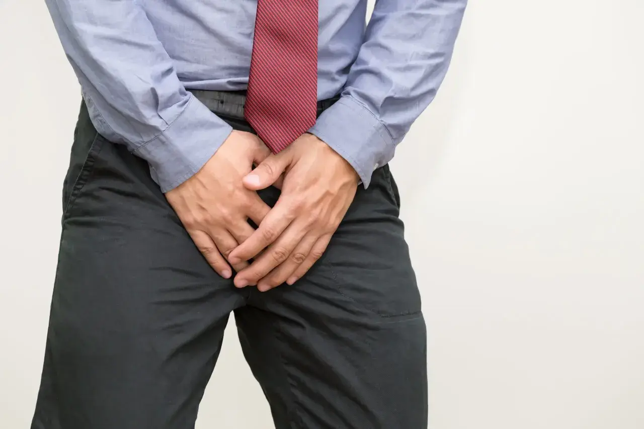 Mann mit Händen vor dem Schritt, der sich unwohl fühlt. Mögliche Ursachen für Blut im Sperma und Hausmittel.