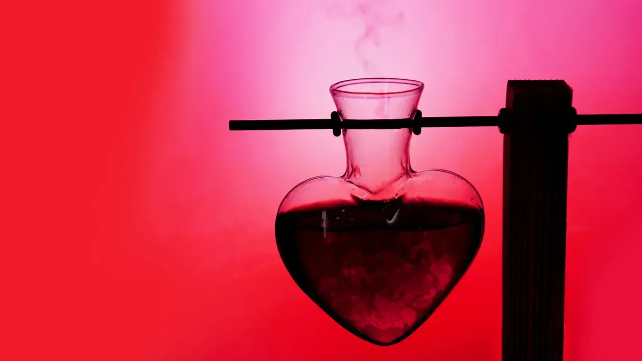 Herzförmige Glasflasche mit dampfender Flüssigkeit, die an ein Liebestrank-Experiment erinnert. Was ist Aphrodisiakum?