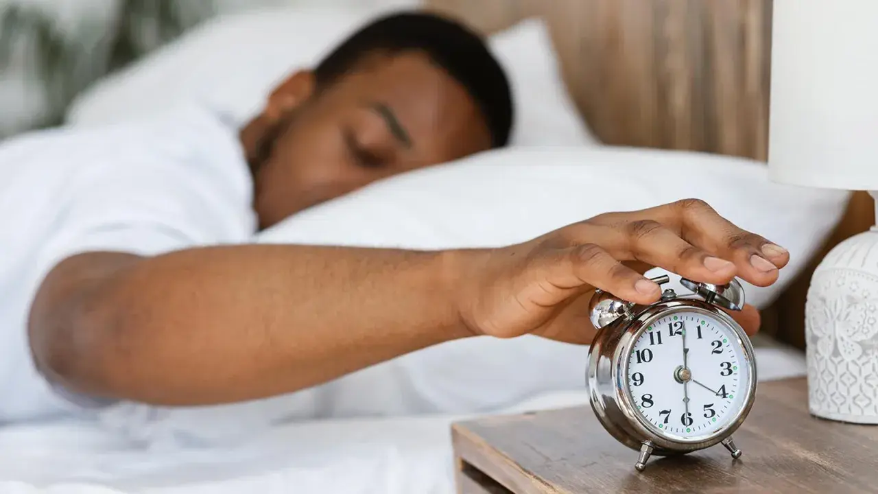 Ein Mann schaltet den Wecker aus. Warum kriegt man eine Morgenlatte? Vielleicht wegen des erholsamen Schlafs, der hier angedeutet wird.