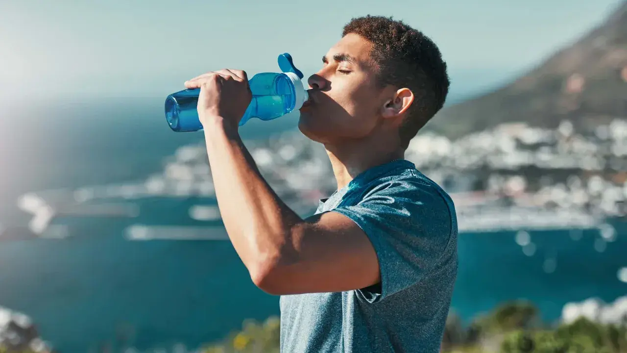 Ein Mann trinkt aus einer blauen Flasche, genießt die Aussicht und das warme Wasser.