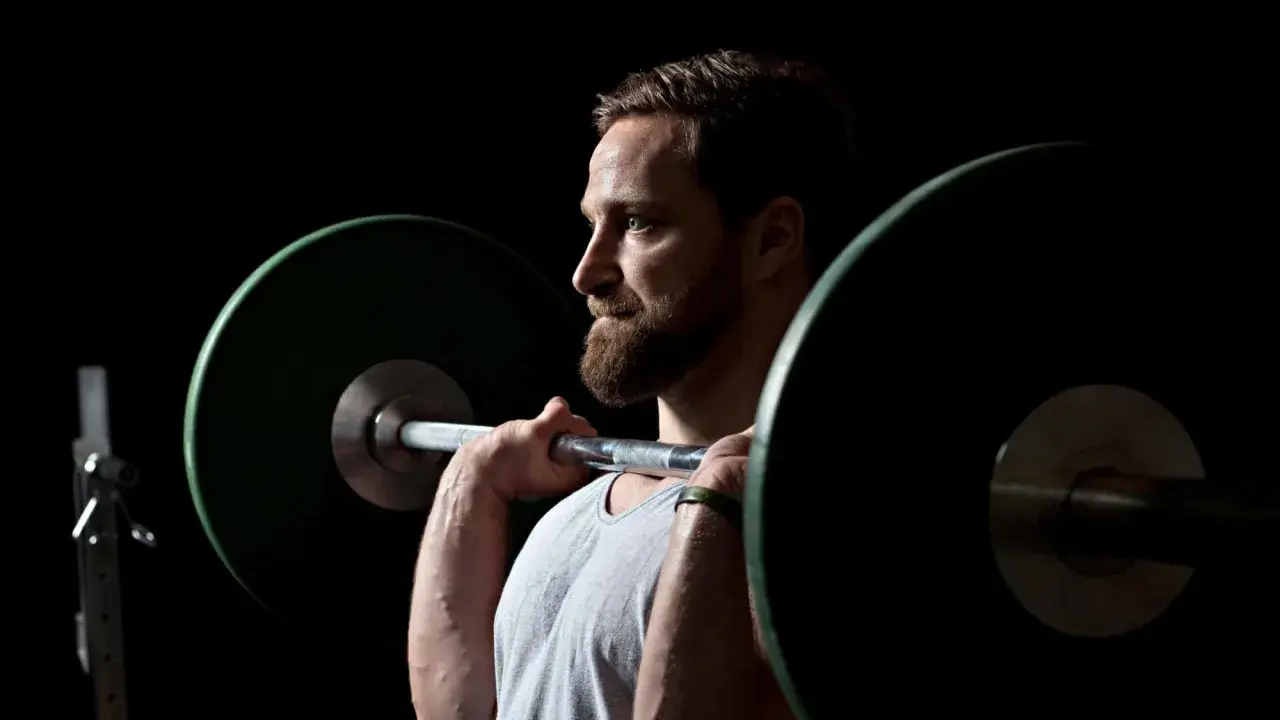 Ein Mann mit Bart hebt eine Langhantel. Er fragt sich, wie oft Krafttraining optimal ist.