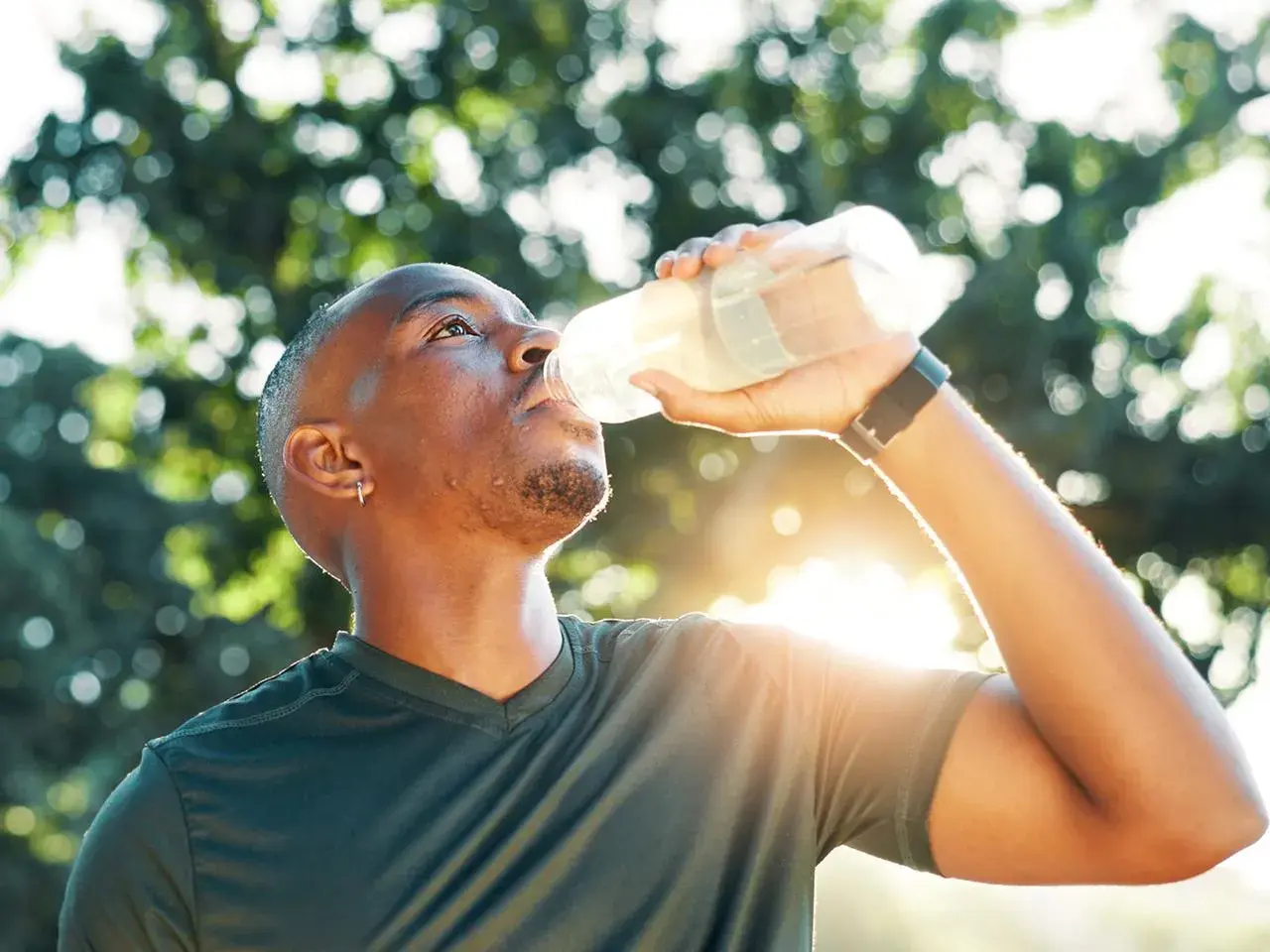 Mann trinkt nach dem Sport aus einer Flasche. Sind Elektrolyte gesund? Ja, sie helfen, den Körper nach Anstrengung zu rehydrieren.