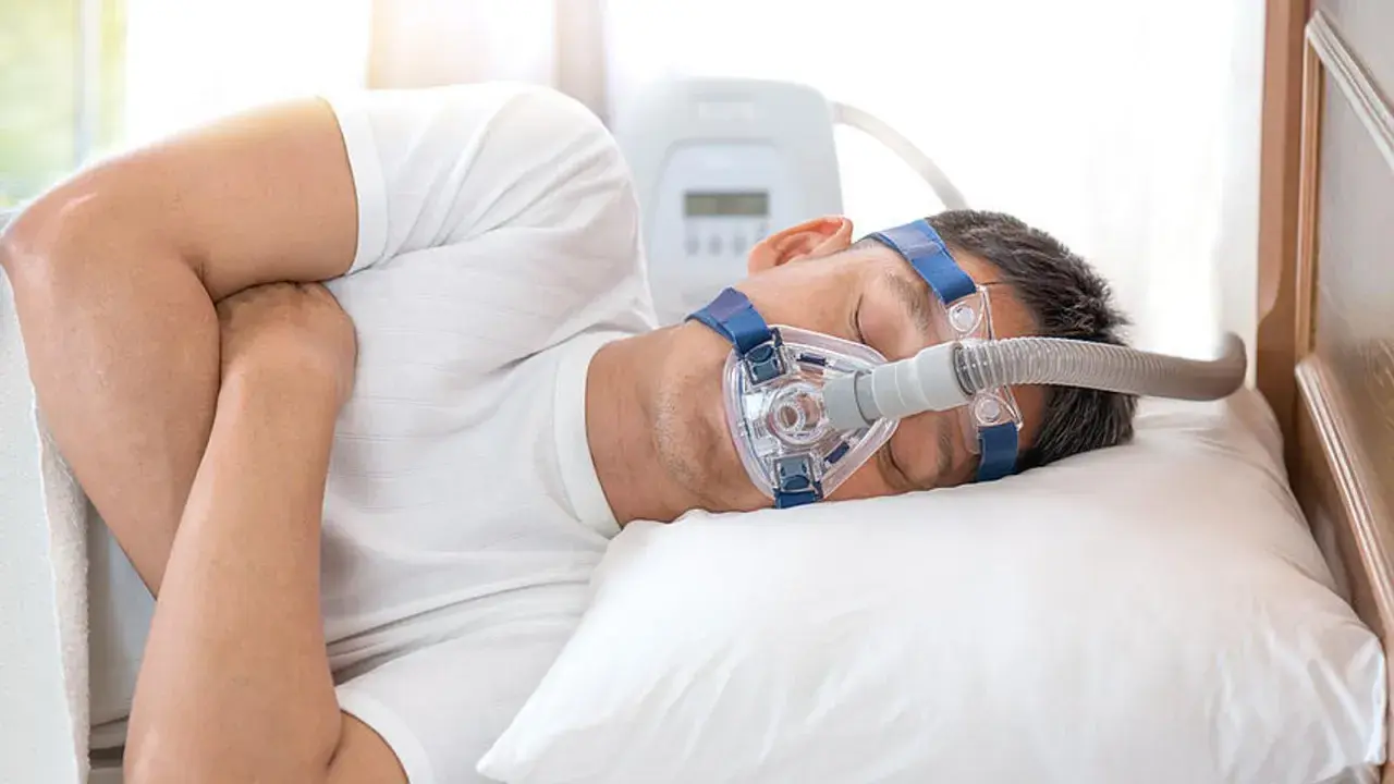 Mann schläft mit CPAP-Maske, um Atemaussetzer am Tag zu behandeln. Ein Gerät unterstützt die Atmung im Schlaf.