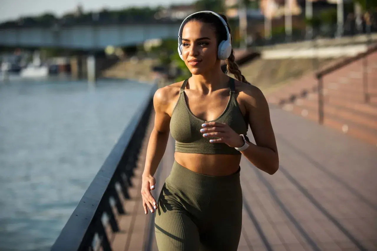 Frau mit Kopfhörern joggt am Wasser entlang. Nach 1 Monat Joggen sieht sie fit und energiegeladen aus.