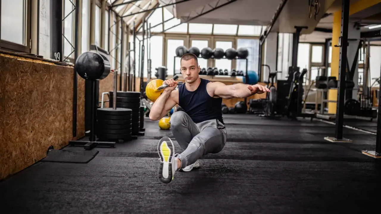 Mann macht einen Pistol Squat mit Kettlebell im Fitnessstudio.