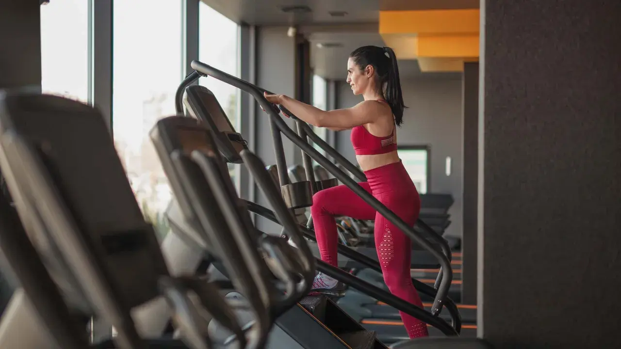 Frau trainiert auf einem Treppensteiger im Fitnessstudio. Was bringt Treppensteigen? Es stärkt Beine und Po, verbessert die Ausdauer und verbrennt Kalorien.