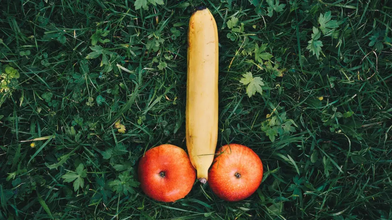 Eine Banane und zwei Äpfel liegen auf grünem Gras und bilden die Form eines kurzen dicken Penis.