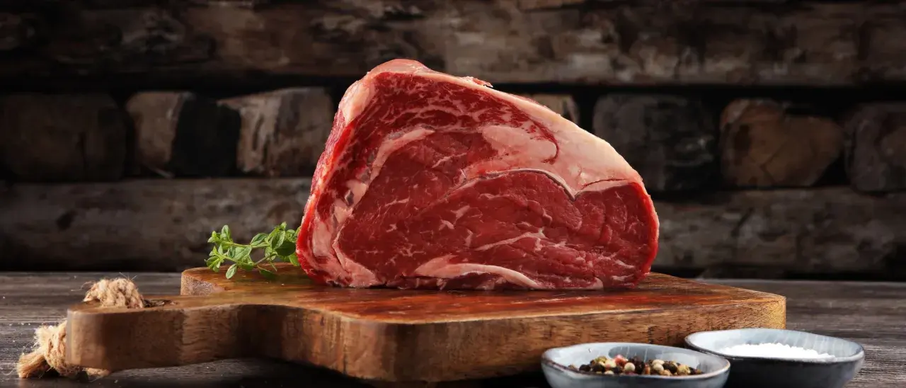 Ein saftiges Stück rotes Fleisch, reich an Eisen, liegt auf einem Holzbrett. Daneben Kräuter und Gewürze.