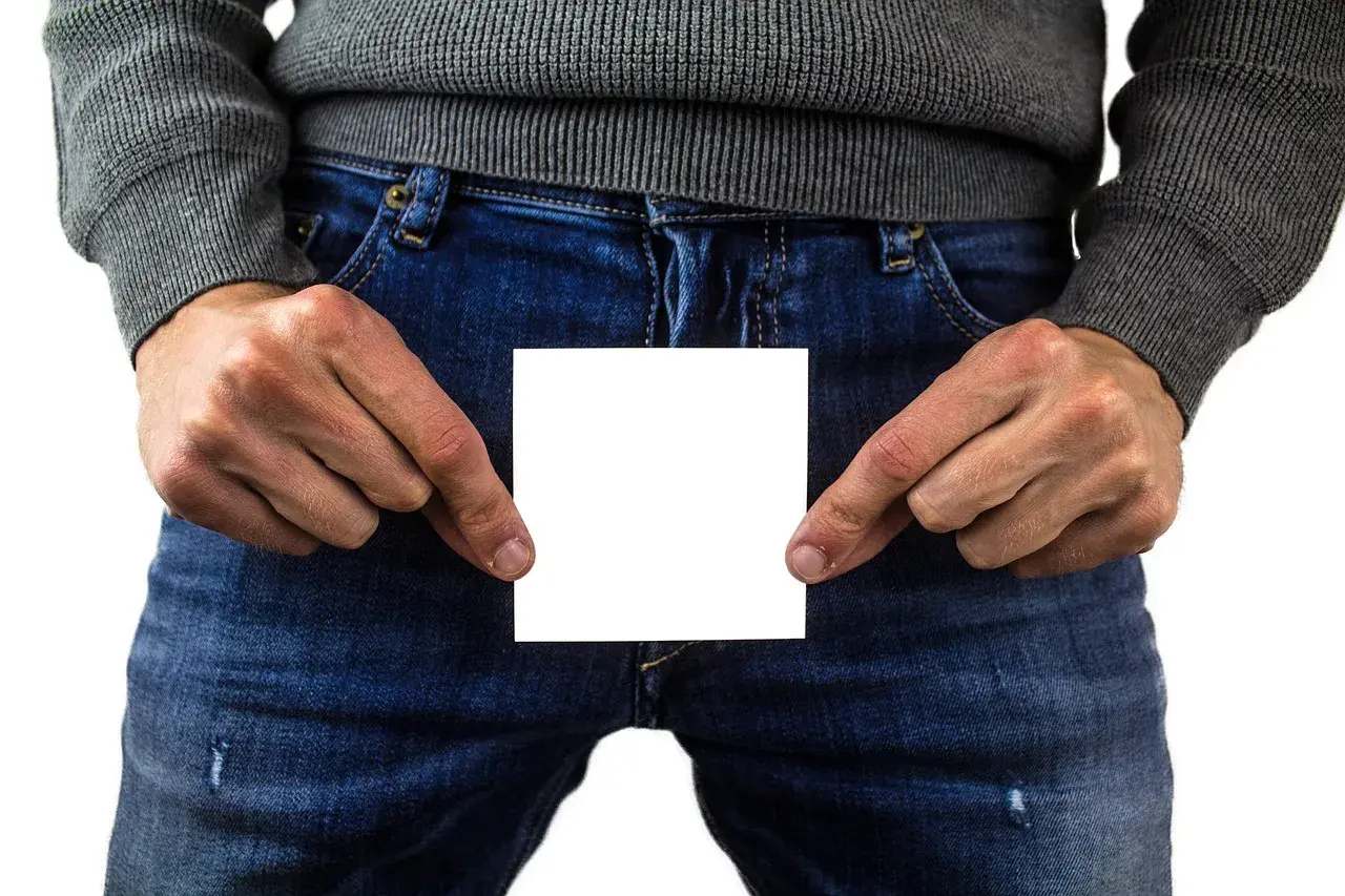 Mann hält ein weißes Blatt Papier vor sich, das eine Beule am Penis verdeckt.