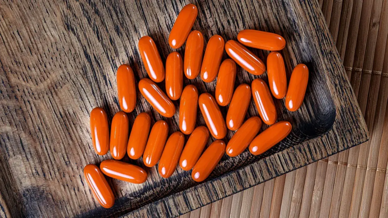 Orange Kapseln mit Beta-Carotin liegen auf einem Holzbrett. Sie könnten Rauchern helfen, ihre Lungen zu schützen.
