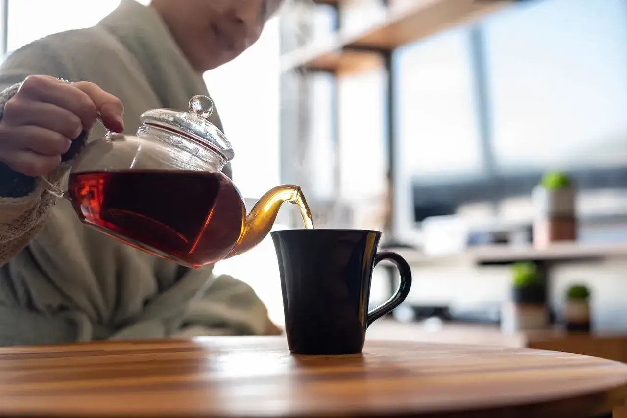 Eine Person gießt schwarzen Tee in eine Tasse. Ist schwarzer Tee gesund? Ja, er ist voller Antioxidantien.