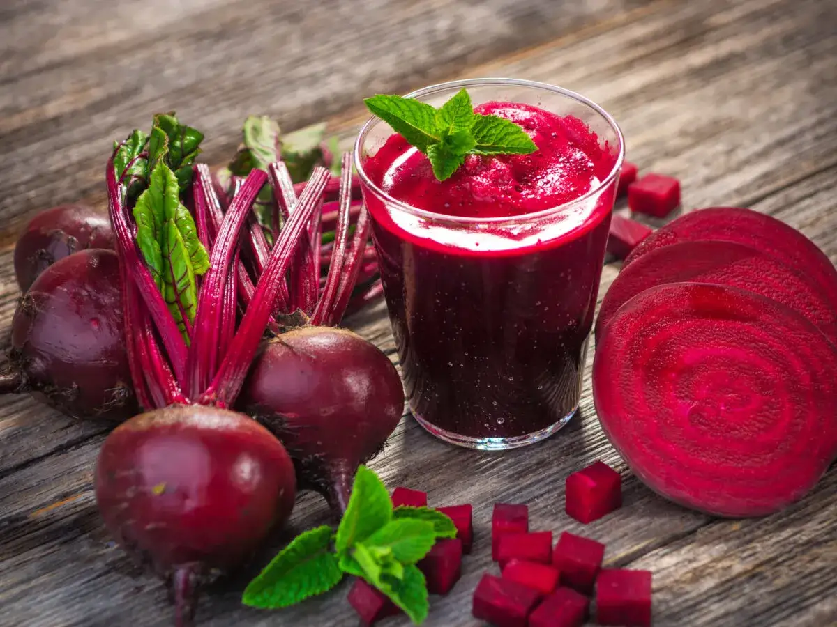 Frischer Rote Bete Saft, der f&uuml;r eine gesunde Erektion sorgen kann, neben ganzen und geschnittenen Rote Bete auf Holz.