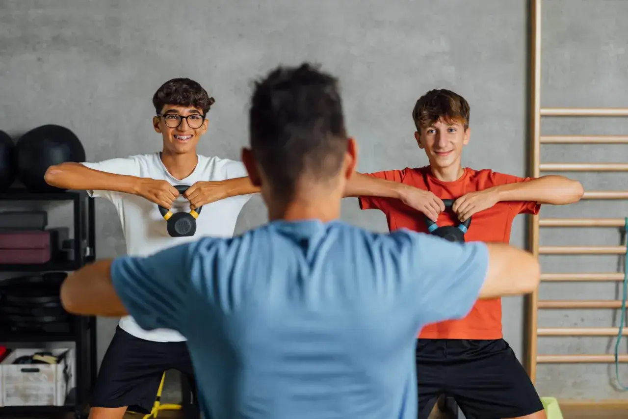 Zwei Jungen trainieren mit Kettlebells im Fitnessstudio. Ab wie vielen Jahren darf man ins Gym? Mit guter Anleitung ist Training für Jugendliche oft schon ab 14 Jahren möglich.