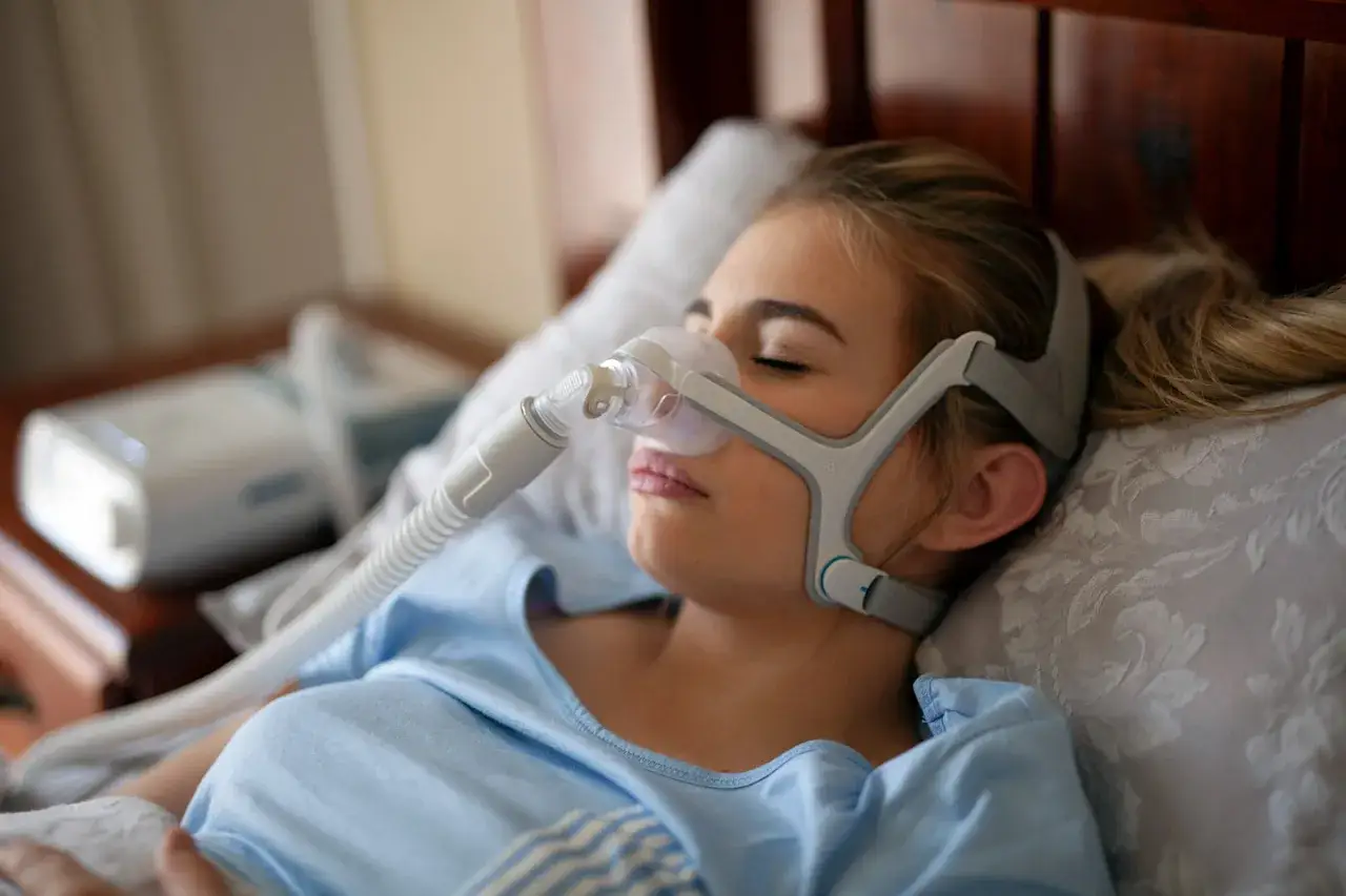 Junge Frau mit Schlafmaske, die gegen Atemaussetzer am Tag hilft. Ein CPAP-Ger&auml;t unterst&uuml;tzt die Atmung im Schlaf.