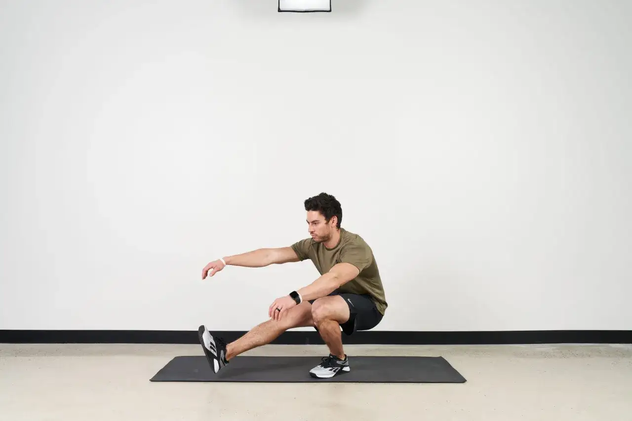 Mann in Sportkleidung macht einen Pistol Squat auf einer Matte. Ein Bein ist ausgestreckt, das andere gebeugt.