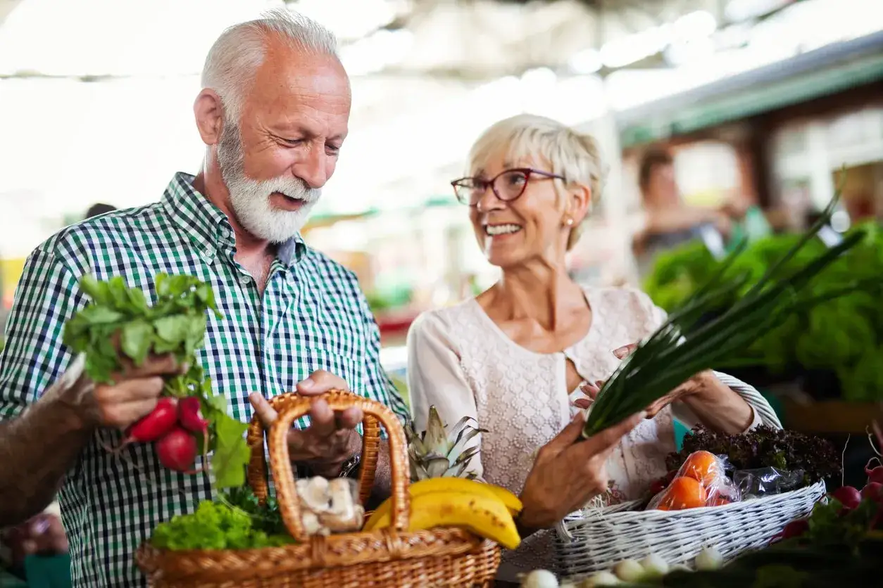 Ein älteres Paar kauft frisches Gemüse. Sie achten auf gesunde Ernährung, wichtig für welche Vitamine ab 80 Jahren.