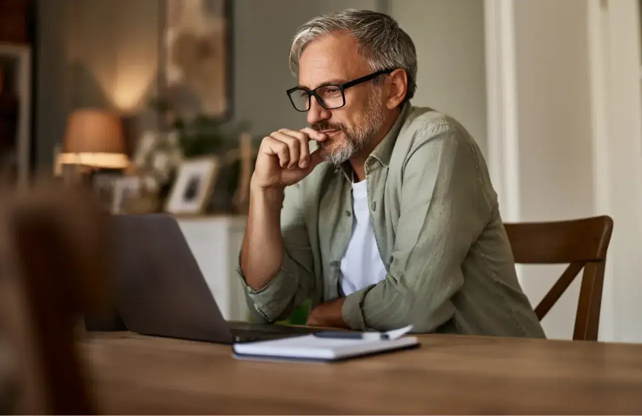 Mann mit Brille denkt nach, vielleicht &uuml;ber erektionsprobleme mit 50. Er sitzt am Laptop.